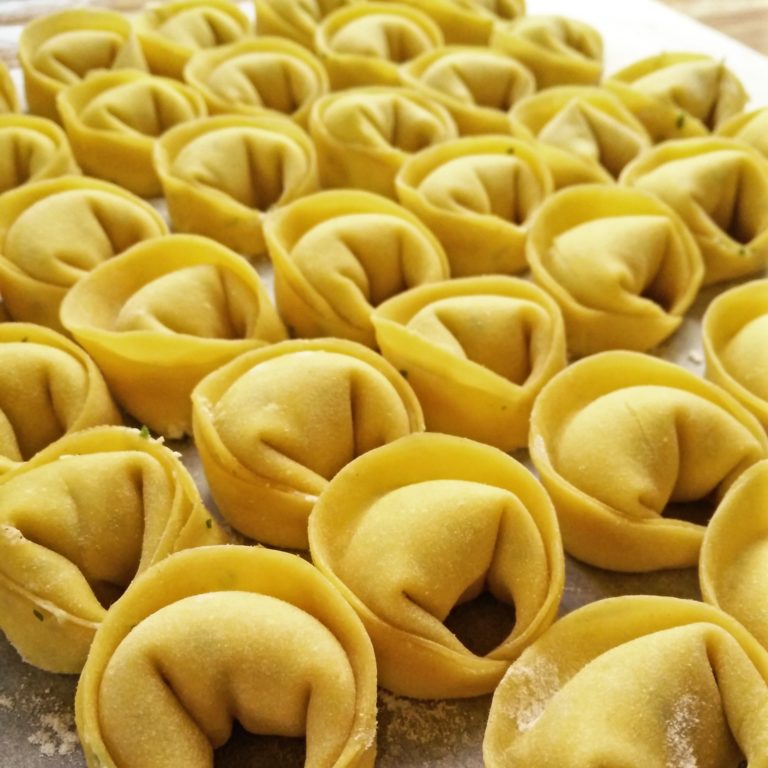Tortelli ripieni crudi disposti su un piano infarinato, visti da vicino