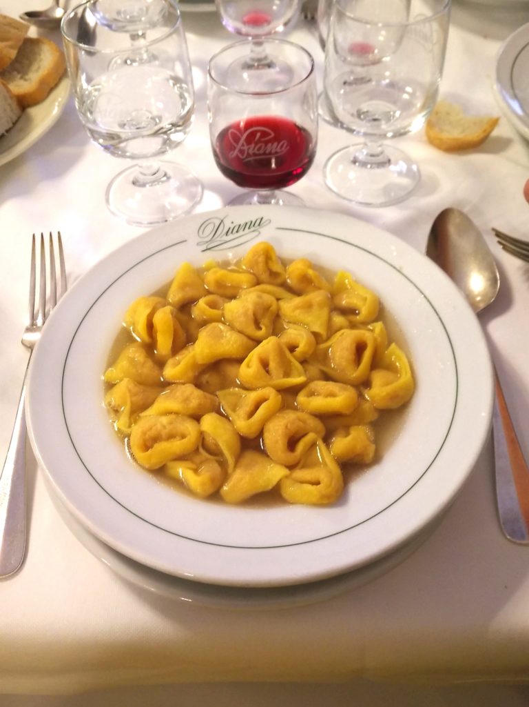 Tortellini in brodo su un piatto del ristorante Diana con calici di vino