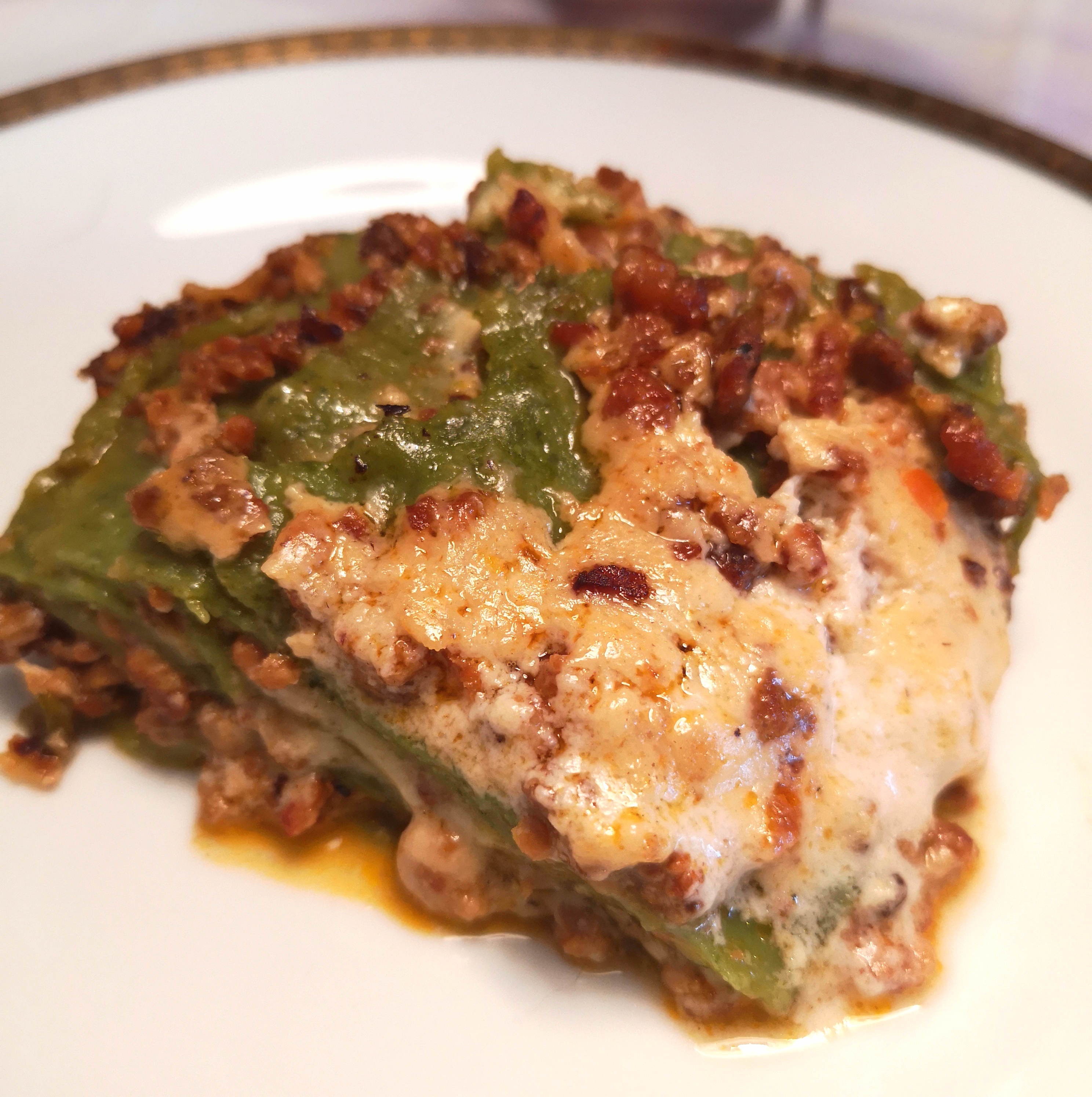 Fetta di lasagna verde al ragù e besciamella su piatto bianco