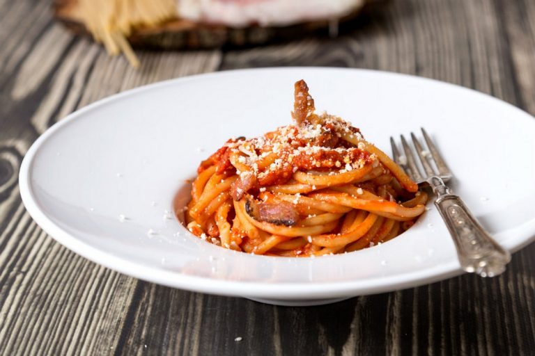 Spaghetti all'amatriciana con guanciale e pecorino grattugiato su piatto bianco