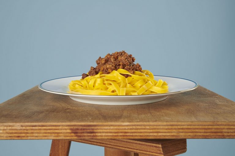 Tagliatelle al ragù su piatto bianco appoggiato su un tavolino di legno