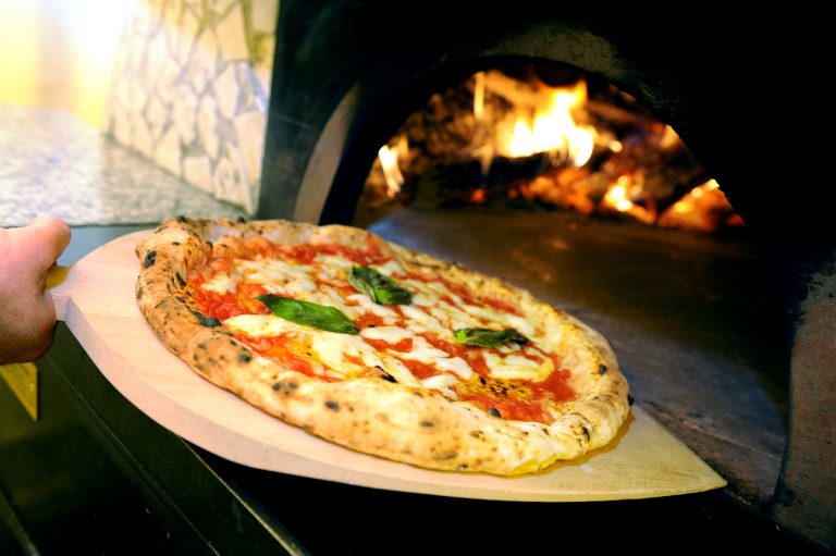 Pizza margherita infornata con la pala in un forno a legna acceso