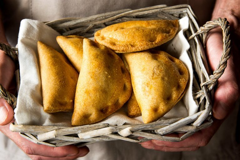 Mani reggono un cestino di vimini con panzerotti fritti dorati