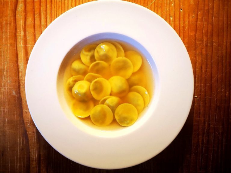 Tortelli tondi in brodo visti dall'alto su piatto bianco