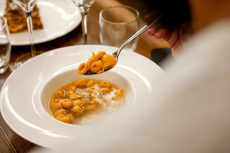 Cucchiaio solleva tortellini in brodo da un piatto fondo bianco