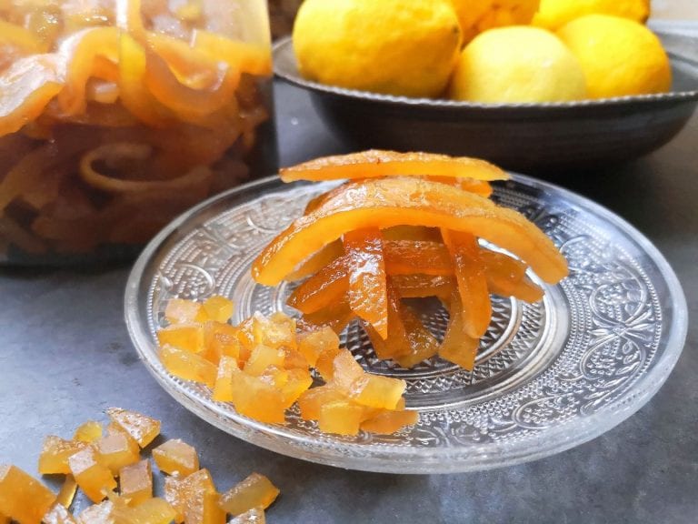 Scorze di arancia candite su un piatto con limoni sullo sfondo