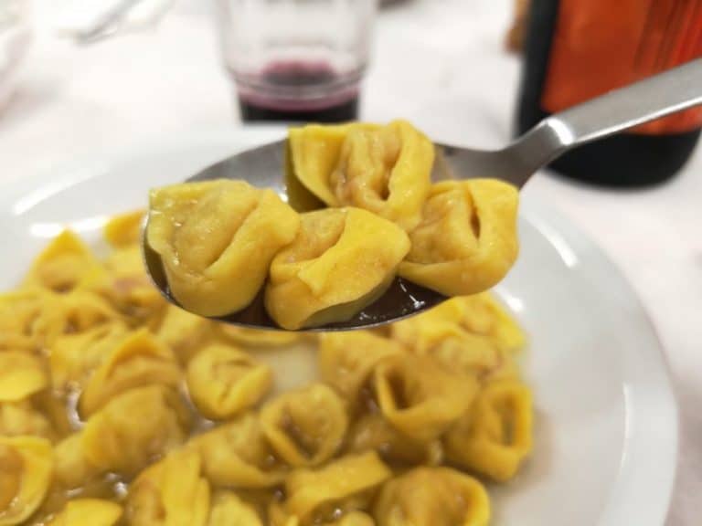 Cucchiaio di tortellini in brodo sollevato da un piatto