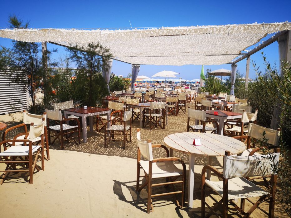 Tavoli e sedie in legno sotto un gazebo ombreggiato in spiaggia